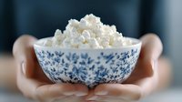 Fresh cottage cheese in traditional porcelain bowl with blue floral pattern held in feminine hands against blurred background, healthy dairy product serving.