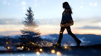 Young woman walking in winter snow at sunset with magical glowing sparkles and pine tree silhouette against mountain landscape background in dreamy atmosphere.