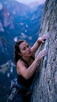 Athletic woman rock climbing on steep cliff face with safety harness against dramatic mountain landscape background during golden hour adventure sports.