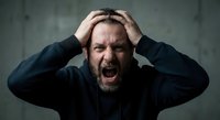 Frustrated middle-aged Caucasian man with beard screaming while holding head in hands expressing stress, anger, mental breakdown, burnout syndrome.
