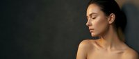 Young woman with closed eyes in peaceful meditation pose against dark background with dramatic lighting for wellness and mindfulness concepts.