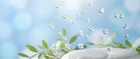 Spa wellness concept with water droplets floating above green leaves and white towel against soft blue sky background for relaxation therapy treatments.