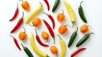 Colorful assortment of fresh hot chili peppers including red, yellow, green and orange varieties arranged on white background for culinary and cooking projects.