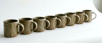 Row of handcrafted ceramic mugs with speckled green glaze arranged in line on white surface for kitchen and dining decor.