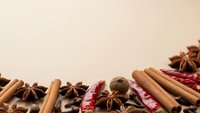 Aromatic spices including cinnamon sticks, star anise, nutmeg and dried chili peppers arranged on neutral background for culinary and cooking projects.