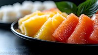 Fresh sliced watermelon and mango arranged on black plate with basil garnish, vibrant tropical fruit composition on dark background, healthy summer food.