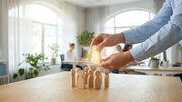 Hands protecting wooden figures in office setting, symbolizing employee care, team support, insurance, and workplace safety for business concepts.