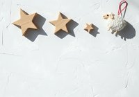 Wooden stars in various sizes and a sheep ornament with red string on white textured surface for holiday decoration and craft projects.