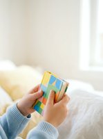 Hands holding colorful Rubik's cube puzzle toy indoors. Child solving logic game with multicolored blocks. Educational toy for problem-solving and cognitive development.