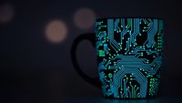 Black coffee mug with glowing blue circuit board pattern on dark background with bokeh lights for tech themed designs and digital concepts.