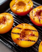 Fresh halved peaches with caramelized grill marks cooking on black grill grates, showing juicy flesh and natural sweetness enhanced by grilling process.
