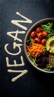 Vegan bowl with avocado, roasted tomatoes, carrots, beets, and greens on dark slate with word vegan written in sauce.