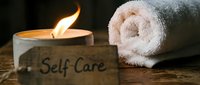 Self care concept with lit candle, rolled white towel, and wooden sign on rustic table, promoting wellness, relaxation, and mindful living.