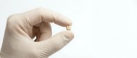 Close-up of a hand holding a small gold pill or capsule against a white background, suitable for pharmaceutical, healthcare, and medical supplement advertising.