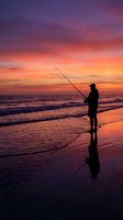 Silhouette of angler fishing at beach during dramatic sunset with vibrant purple orange sky reflecting on wet sand and ocean waves for outdoor recreation concepts.