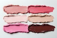 Smeared makeup swatches in pink and brown tones on white background, showing texture and consistency of cosmetic products for beauty industry use.