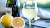 Refreshing glass of white wine with fresh cut lemons on blue background, selective focus on wineglass with condensation drops, summer drink concept.