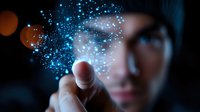 Magical glowing blue particles floating above finger of young Asian man in dark setting, creating ethereal atmosphere for technology and innovation concepts.