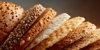 Assorted sliced bread loaves with various seeds and grains, showcasing different textures and crusts in warm, appetizing lighting.