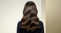 Woman with long wavy brown hair from behind showing healthy shiny locks against neutral background for hair care and beauty concepts.