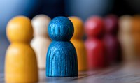 Wooden pawn figures in different colors standing in row with blue figure in focus, symbolizing leadership, diversity and teamwork concept in business setting.