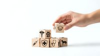 Hand placing wooden cube with recycling symbol onto stack of eco-friendly blocks featuring environmental icons on white background.