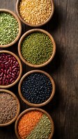 Assorted legumes and pulses in wooden bowls on rustic wood surface, including lentils, chickpeas, beans and peas for cooking and nutrition.