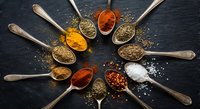 Colorful spices and herbs arranged in wooden spoons on dark slate background. Culinary ingredients for cooking and seasoning food preparation.