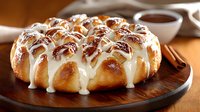 Fresh baked cinnamon rolls with sweet cream cheese frosting drizzle arranged on wooden serving board, warm golden brown dough and gooey white topping.