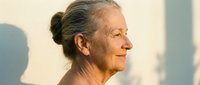 Senior woman with gray hair in bun, smiling in profile against warm sunlight. Mature female portrait for wellness, aging, healthcare, and lifestyle content.