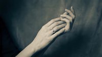 Elegant female hands with a silver ring against a dark textured background, evoking romance, engagement, and timeless love.