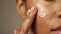 Young woman applying moisturizer cream on face with finger, skincare routine for healthy glowing skin and anti-aging beauty treatment.