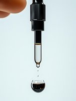 Dropper with dark liquid medicine dripping into glass sphere against light background. Minimalist pharmaceutical composition showing precise dosing and measurement.
