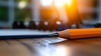 Sharpened orange pencil on wooden surface with blurred office background and warm sunlight, suitable for education and creativity concepts.