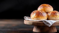 Fresh homemade brioche buns with glossy golden crust on wooden cake stand against dark background, soft natural lighting creates appetizing mood.