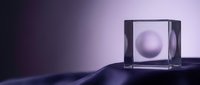 Translucent glass cube with floating sphere inside on dark wavy surface, minimalist composition with purple and blue lighting for modern design projects.