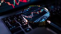 Magnifying glass on laptop keyboard examining stock market candlestick chart data analysis with red and green trading indicators in dark environment.