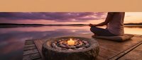 Peaceful meditation session at sunset with candle burning in stone bowl on wooden dock overlooking calm lake waters during golden hour twilight.