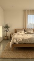 Minimalist bedroom with wooden bed, linen bedding, jute rug, potted olive tree, and sheer curtains in warm neutral tones.