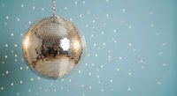 Shiny silver disco ball hanging against soft blue background with sparkling bokeh lights creating festive party atmosphere for celebrations and events.