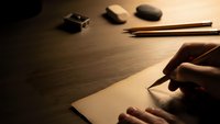 Hand writing on blank paper with pencil in warm lighting on wooden desk with eraser and sharpener for creative writing and artistic expression.