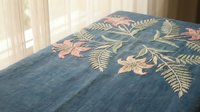 Blue denim fabric with colorful floral embroidery featuring pink flowers and green leaves in decorative pattern for textile and fashion design projects.