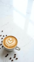 Overhead view of cappuccino with latte art in white ceramic cup surrounded by scattered coffee beans on marble surface, ideal for cafe and beverage marketing.