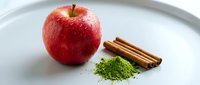 Red apple with cinnamon sticks and matcha powder on white plate for food styling, nutrition, wellness, and culinary design projects.