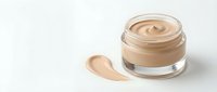 Open glass jar of beige foundation cream with smooth swirl texture and makeup smear sample on white background for cosmetic product advertising.