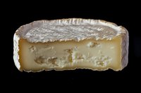 Creamy French soft cheese with white mold rind cut in half showing smooth interior texture and ripened edges against black background, isolated food photography.