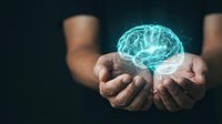 Glowing digital brain hologram floating above cupped hands representing artificial intelligence, neuroscience, and mental health concepts.