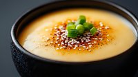 Creamy butternut squash soup garnished with sesame seeds and fresh chopped green onions served in black ceramic bowl on dark background. Perfect for food blogs.