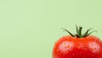 Fresh red tomato with water droplets on light green background for healthy eating and cooking concepts.