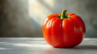 Fresh ripe red tomato with green stem on wooden table in soft natural light, dramatic side lighting creates gentle shadows and highlights glossy skin.